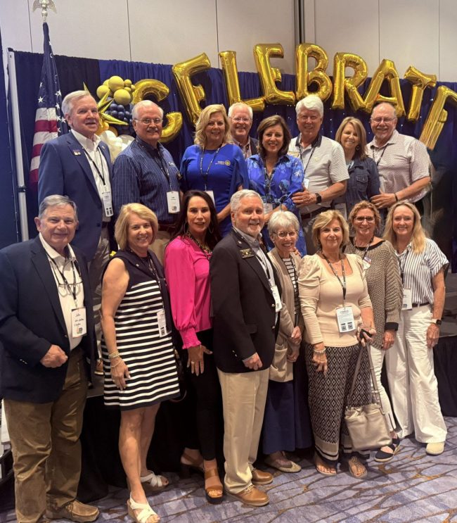 Group of adults posing for a group photo at a conference, with gold 'Celebrate' balloons and an American flag in the background.