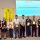 Nine award recipients pose with plaques at an awards presentation, with a Rotary banner and an 'Awards Presentations' slide behind them.