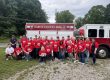 Group of people in red shirts posing in front of a Rabun County Fire engine.