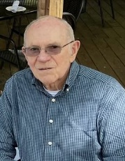 image9 - Rotary Club Of Clayton Older man with short white hair and glasses, wearing a blue checkered button-up shirt, seated on a wooden porch.
